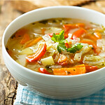 A vertical, top-down shot of a vibrant, chunky cabbage soup in a rustic bowl with a gold spoon, surrounded by fresh herbs like parsley and celery