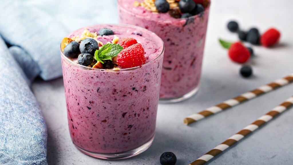 Berry protein smoothie topped with blueberries, raspberries, mint, and nuts in a clear glass.