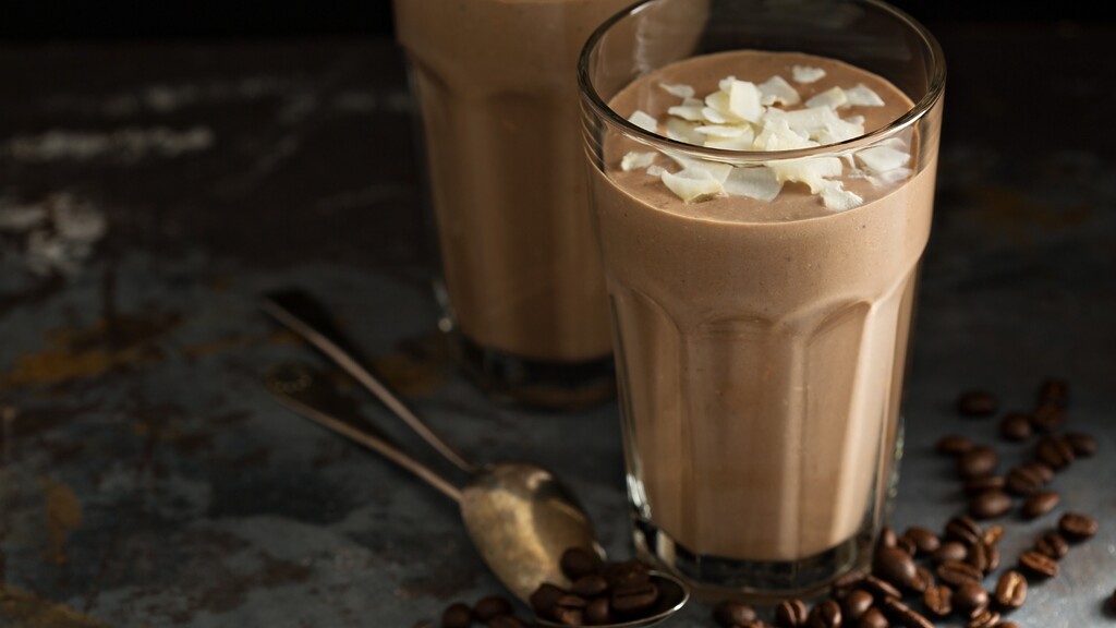 Chocolate coffee protein smoothie topped with coconut flakes, served with coffee beans on a dark table.