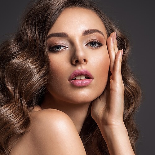 Woman with voluminous brunette waves wearing soft glam makeup, pink lips, defined brows, and luminous skin