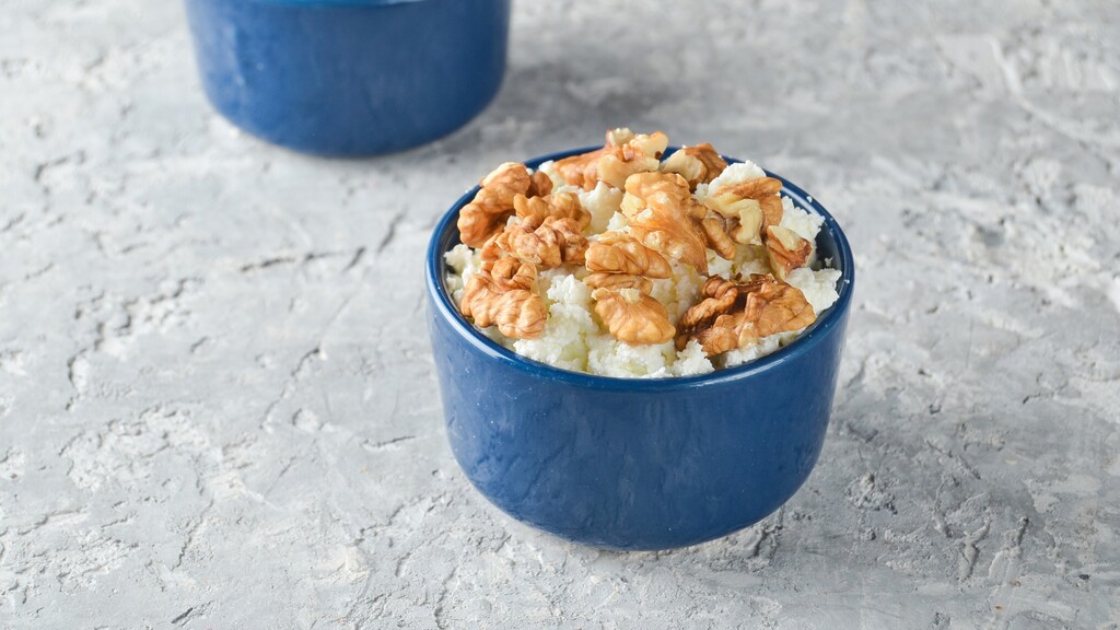 Small bowl of cottage cheese topped with walnuts on a light stone surface
