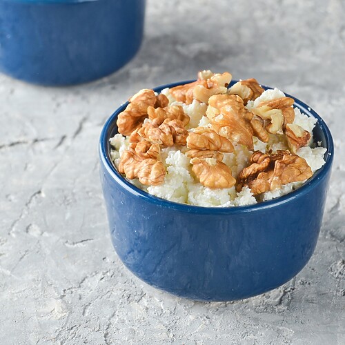 Small bowl of cottage cheese topped with walnuts on a light stone surface