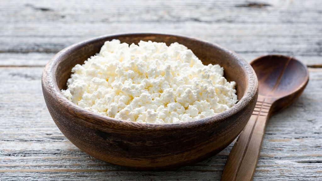 Bowl of cottage cheese on a rustic wooden table with a wooden spoon.