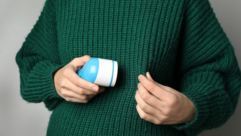 Fabric shaver removing pills from a green knit sweater.