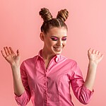 10 Easy Space Buns Hairstyles to Rock at Any Hair Length Smiling woman with double space buns hairstyle wearing a pink shirt against a pink studio background.