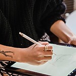 10 Unique Tattoo Ideas That Actually Tell Your Story Person with forearm tattoos sketching a custom tattoo design on a digital tablet with a stylus.
