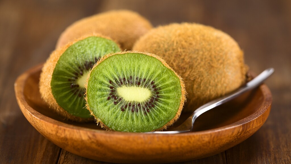 Sliced kiwi fruit in a wooden bowl with a spoon beside it