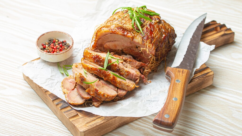 Sliced roasted turkey breast on a cutting board with herbs and pepper
