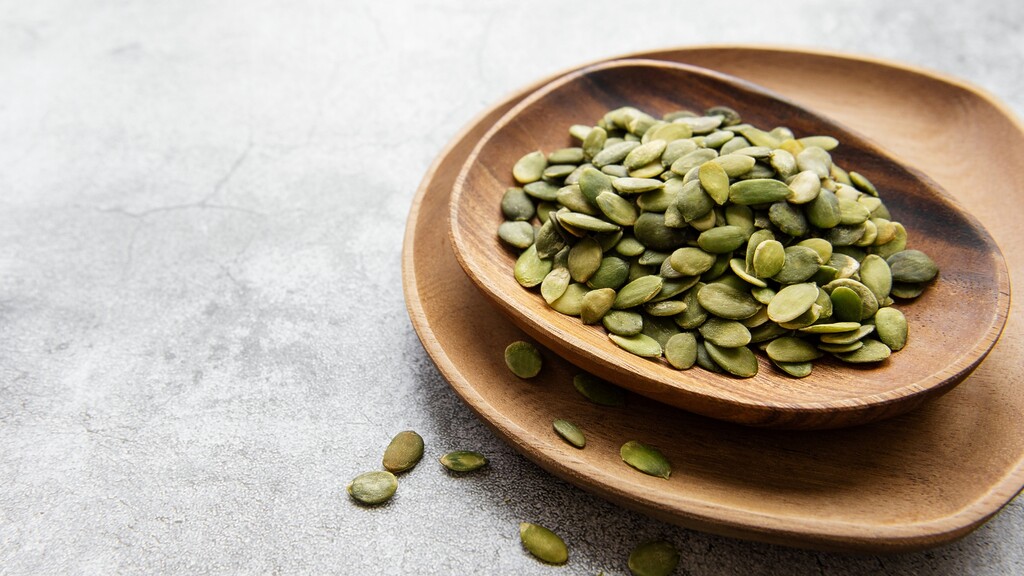 Pumpkin seeds in a wooden bowl on a light stone surface.