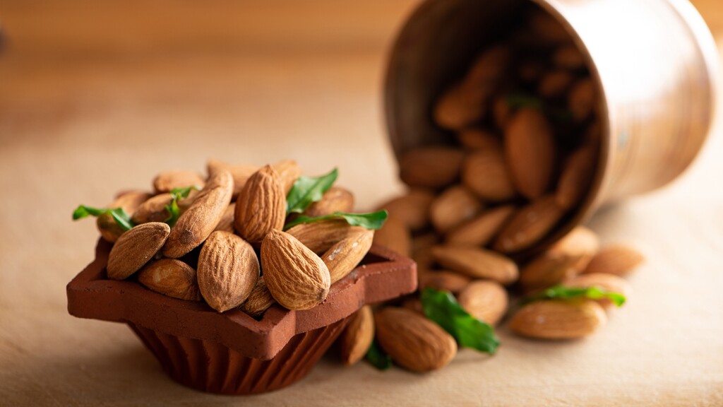 Raw almonds spilling from a small cup onto a wooden surface.
