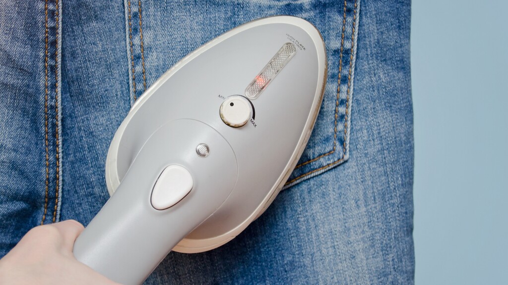 Handheld steamer pressing a crease into denim jeans.