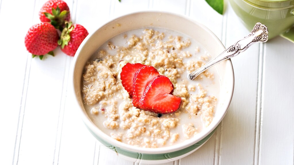 Bowl of oatmeal with milk and sliced strawberries on a white breakfast table.