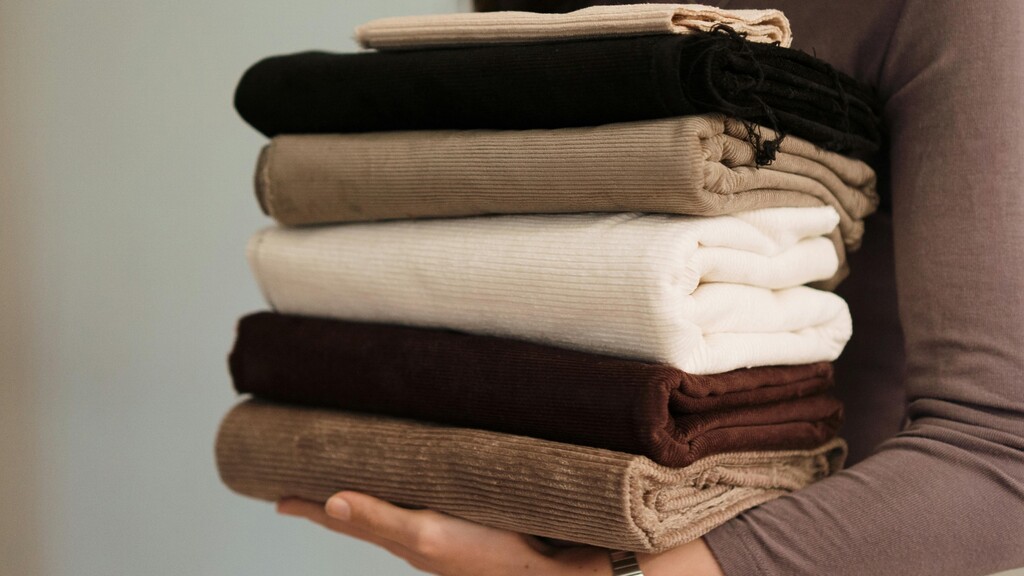 Stack of folded neutral fabrics showing matte textures in cream, brown, and black.