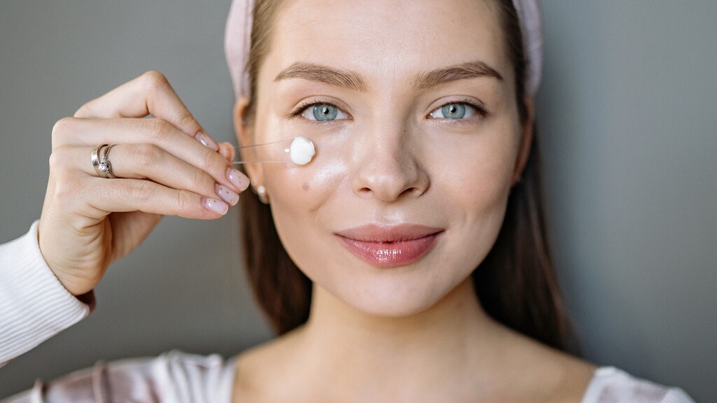 Woman applying moisturizer to her cheek as part of a skin prep routine before makeup.