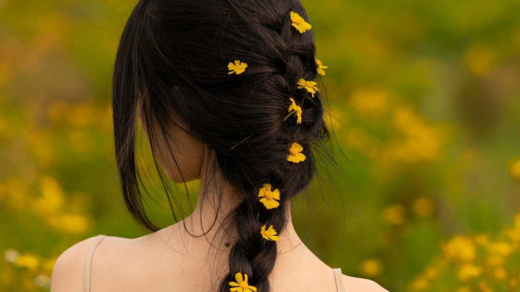 Loose dark braid decorated with small yellow flowers in a green field.