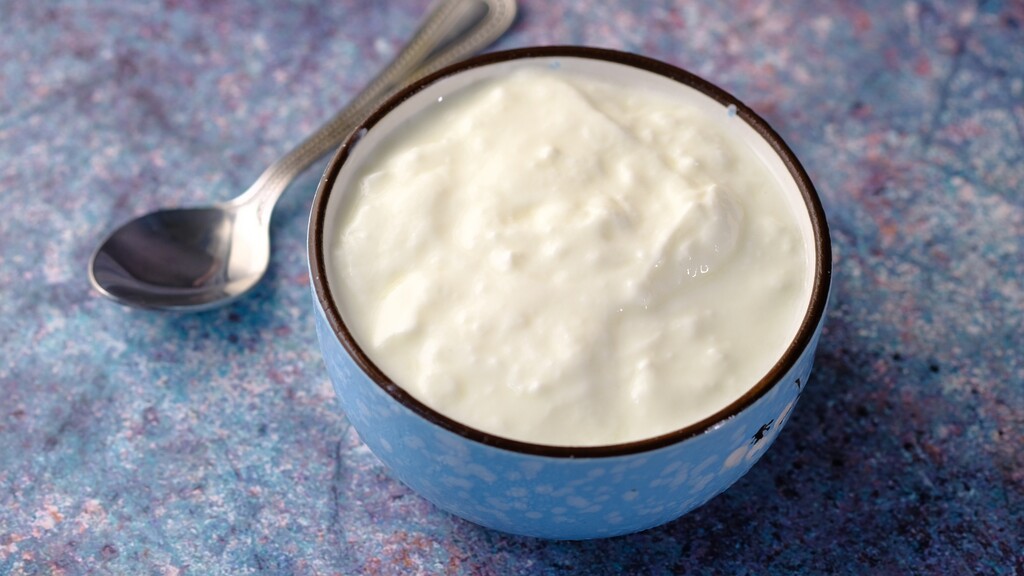 Bowl of plain Greek yogurt with a spoon on a blue textured surface