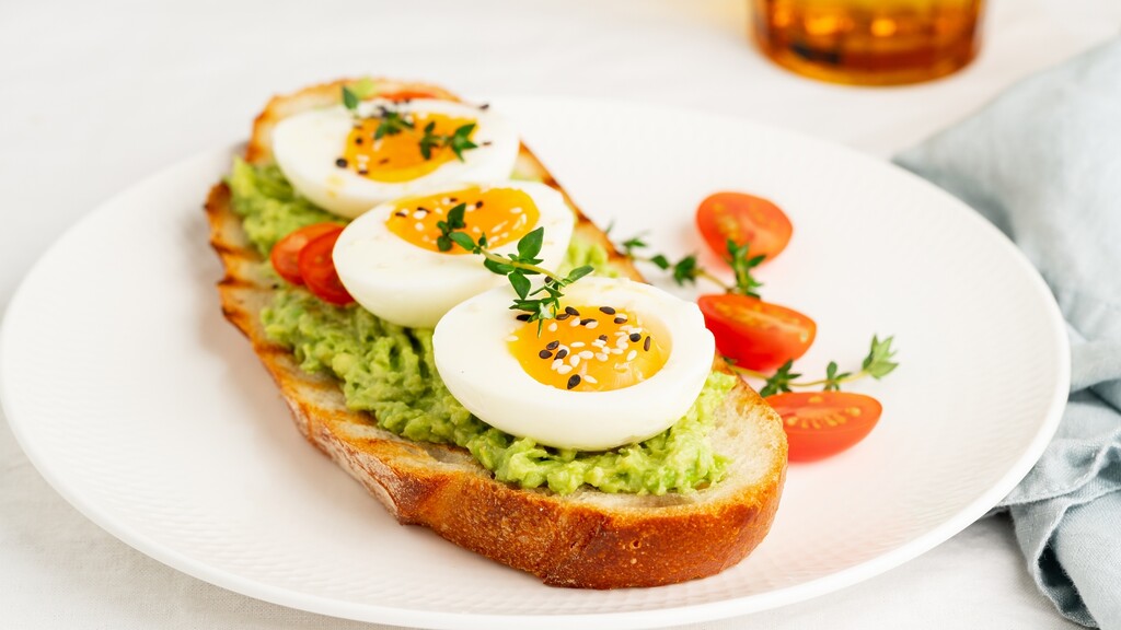 Soft-boiled eggs on avocado toast with cherry tomatoes and herbs.