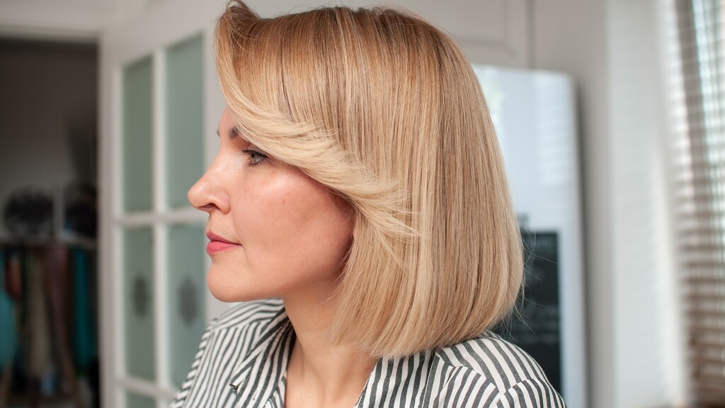 Blonde woman with a smooth collarbone bob and side-swept layers that frame the face.