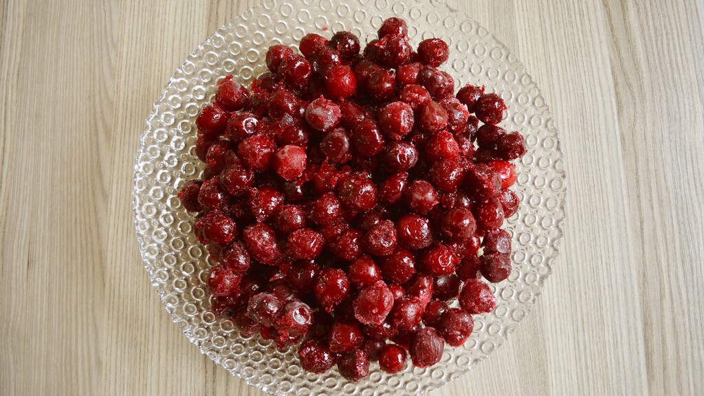 Frozen tart cherries on a clear glass plate over a light wooden table.