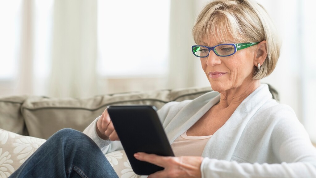 Older woman with a short blonde bob and light bangs using a tablet at home.