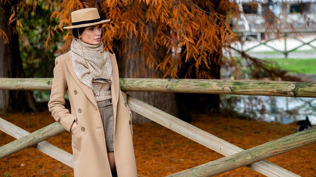 Woman in a camel coat and neutral accessories for an elegant monochrome outfit.