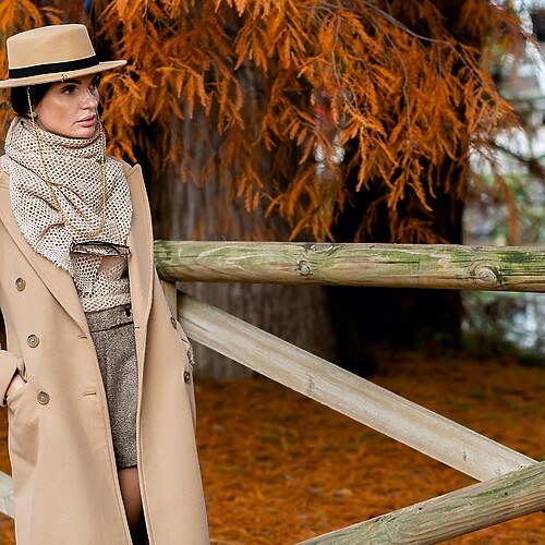 Woman in a camel coat and neutral accessories for an elegant monochrome outfit.