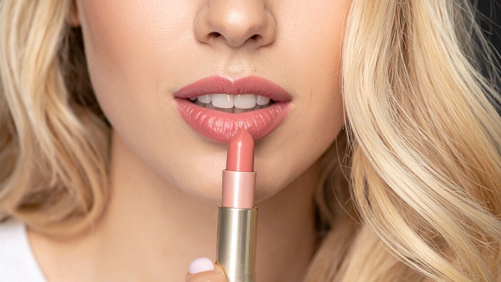 Close-up of a woman applying nude pink lipstick for a soft, polished makeup look.