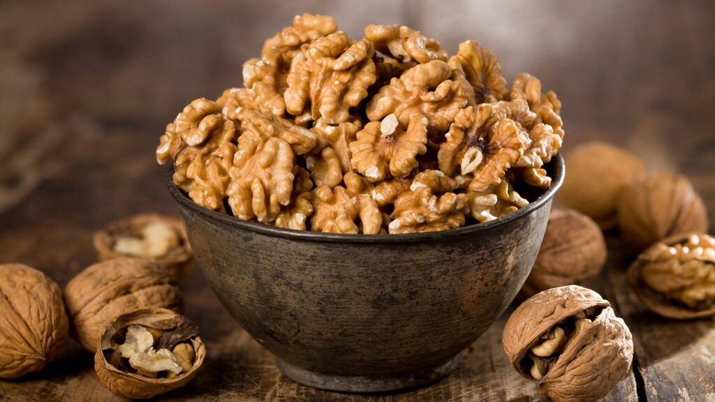 Bowl of walnut halves with whole walnuts scattered on a rustic wooden surface.