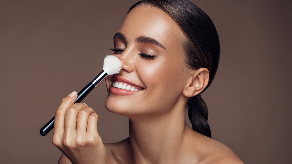 Woman applying face powder with a large makeup brush for a smooth finished complexion.