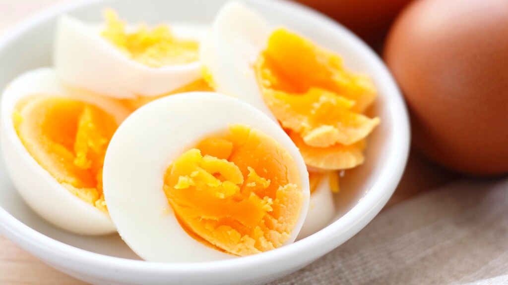 Sliced hard-boiled eggs in a white bowl with whole eggs in the background.