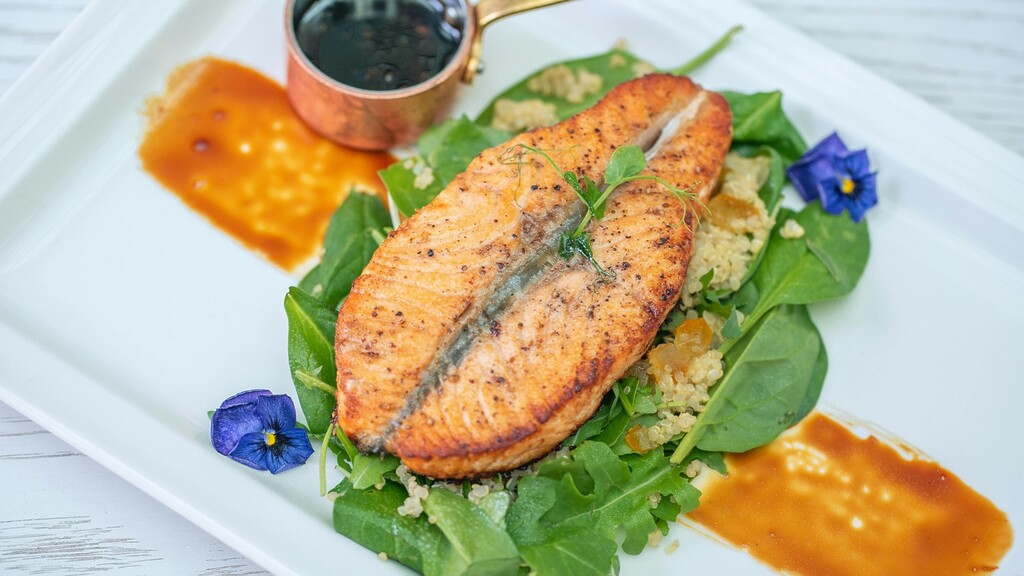 Grilled salmon fillet served over spinach and grains on a white plate.
