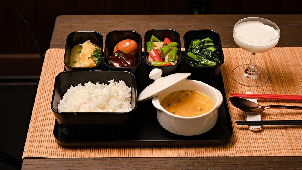 Japanese-style meal with rice, soup, vegetables, small side dishes, chopsticks, and a cultured drink on a dining table.