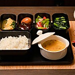 Japanese-style meal with rice, soup, vegetables, small side dishes, chopsticks, and a cultured drink on a dining table.