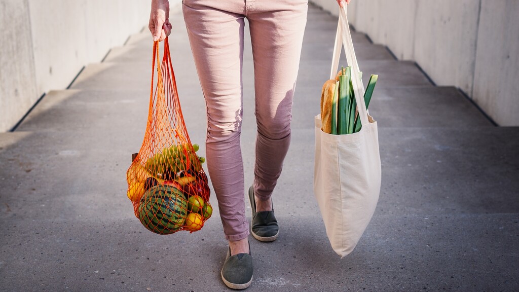 Person walking with reusable grocery bags filled with fresh produce, showing simple daily movement as part of a healthy lifestyle.