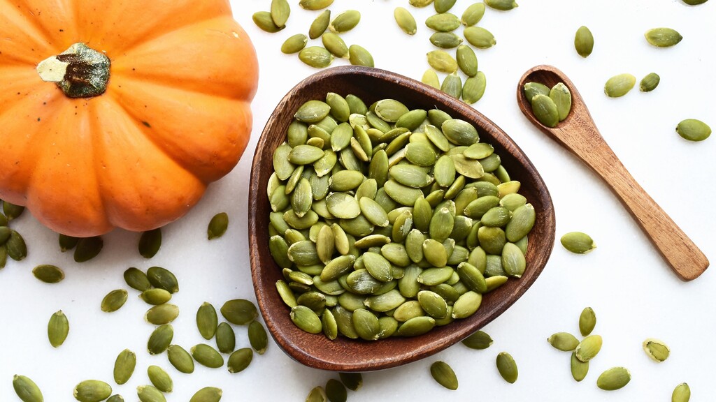 Shelled pumpkin seeds scattered around a wooden bowl and spoon