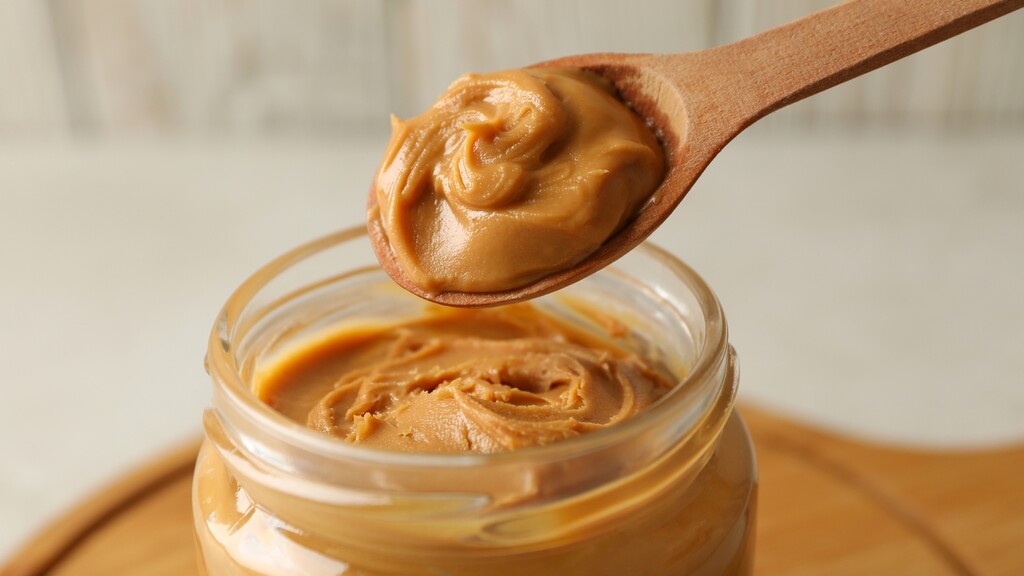 Wooden spoon lifting natural peanut butter from a glass jar