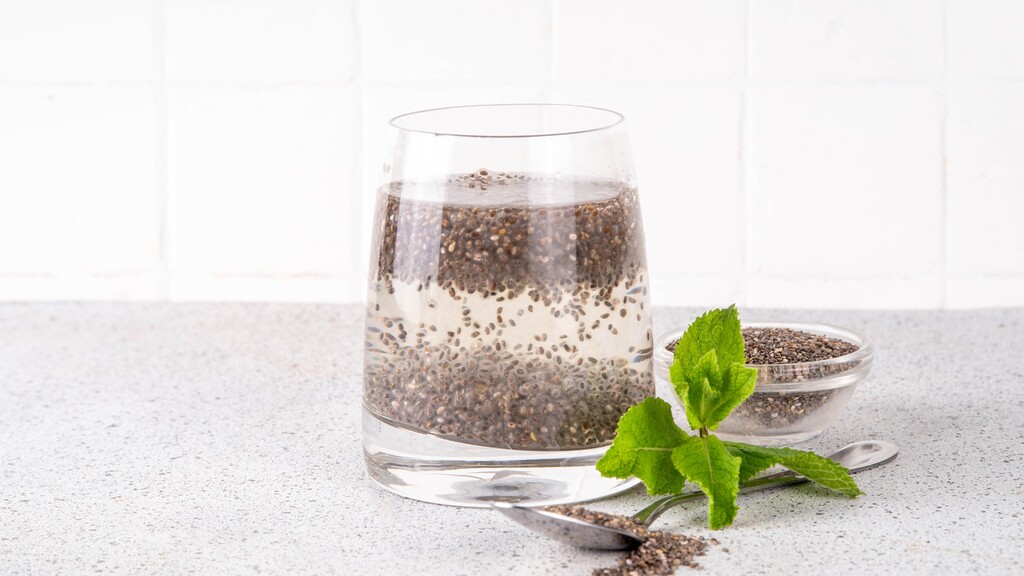 Chia seeds soaking in water with fresh mint and a spoon of dry seeds.