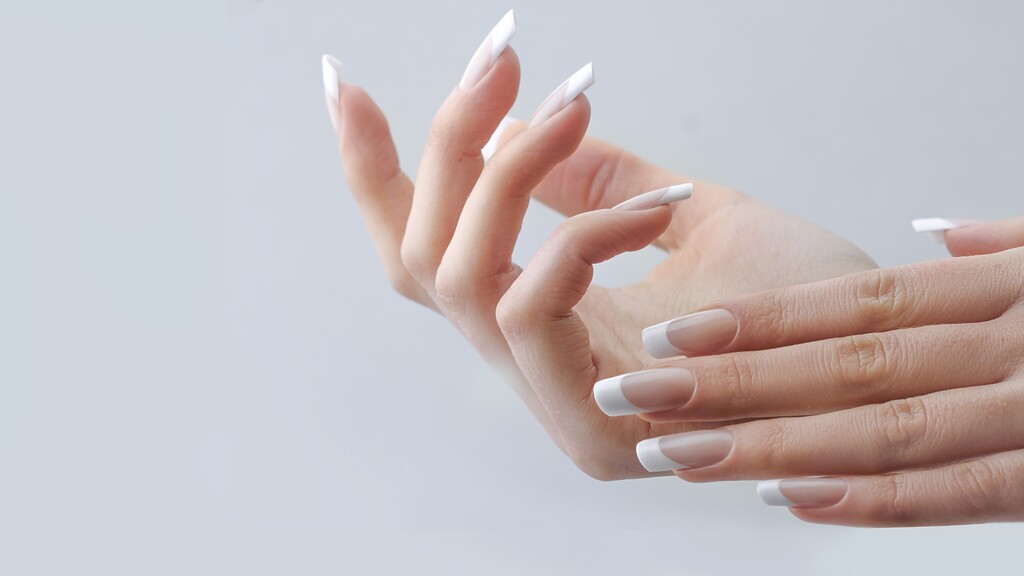 Close-up of hands with long square French tip nails on a soft gray background.