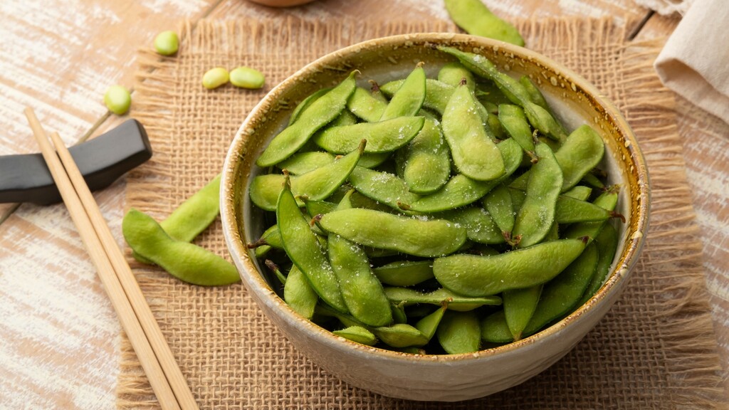 Bowl of steamed edamame pods sprinkled with salt on a rustic table.