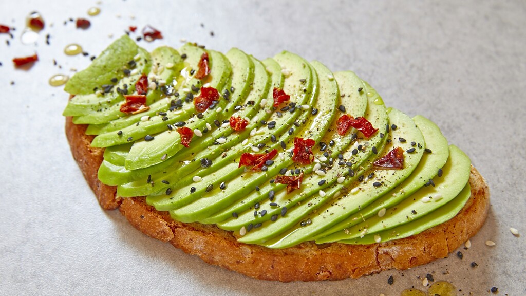 Sliced avocado toast topped with seeds, chili flakes, and olive oil.