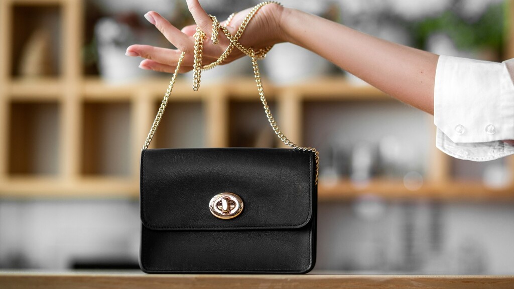Structured black handbag with a gold chain handle held as a refined accessory.