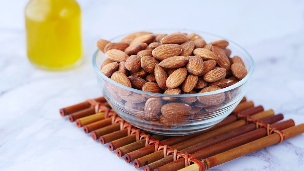 Glass bowl filled with almonds on a bamboo mat with a small bottle in the background