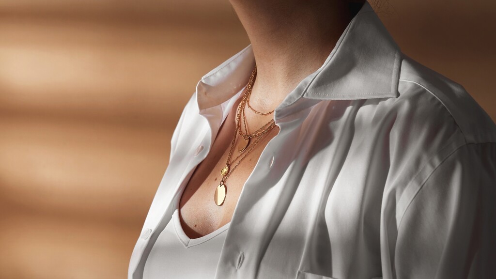 Delicate layered gold necklaces worn with a crisp white shirt.