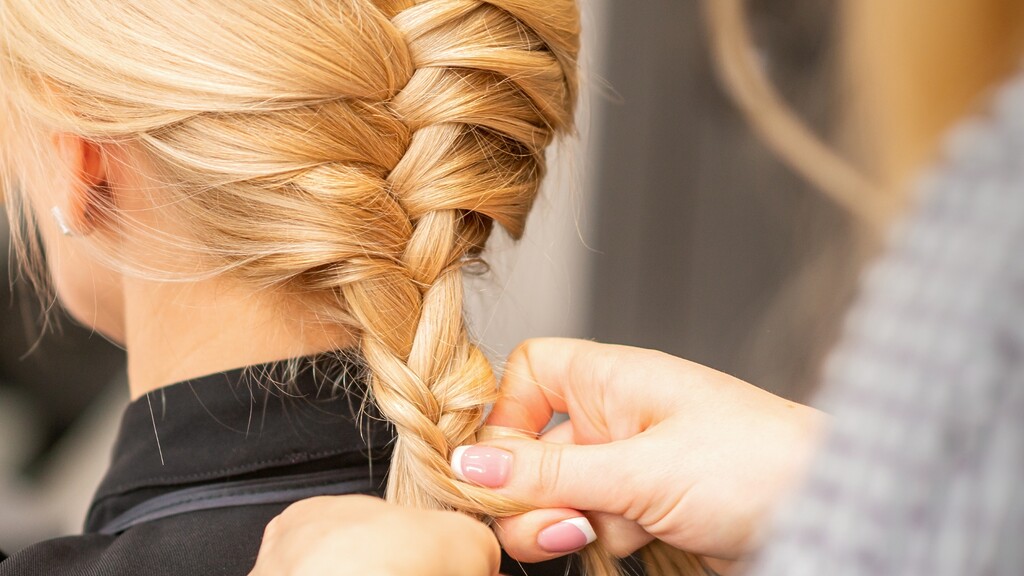 Close-up of blonde hair being woven into a loose side braid by a stylist.