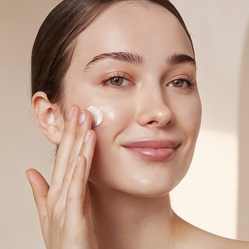 Woman applying moisturizer or hydrating foundation to her cheek, showing smooth, glowing skin for a dry skin makeup routine.