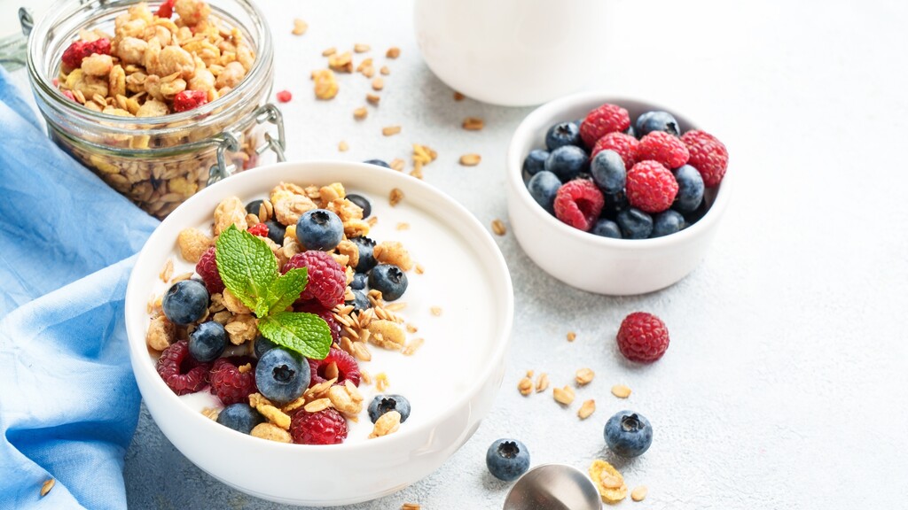 Greek yogurt bowl topped with granola, blueberries, raspberries, and fresh mint.