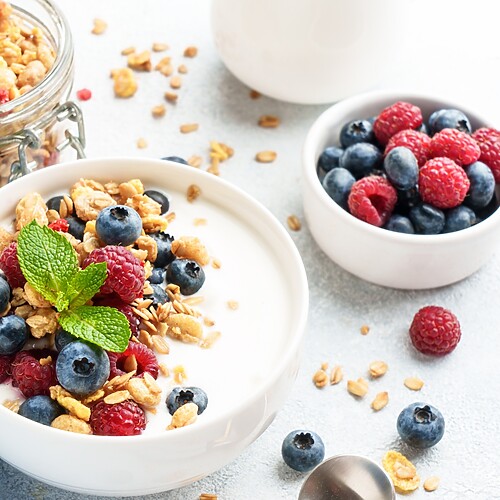 Greek yogurt bowl topped with granola, blueberries, raspberries, and fresh mint.