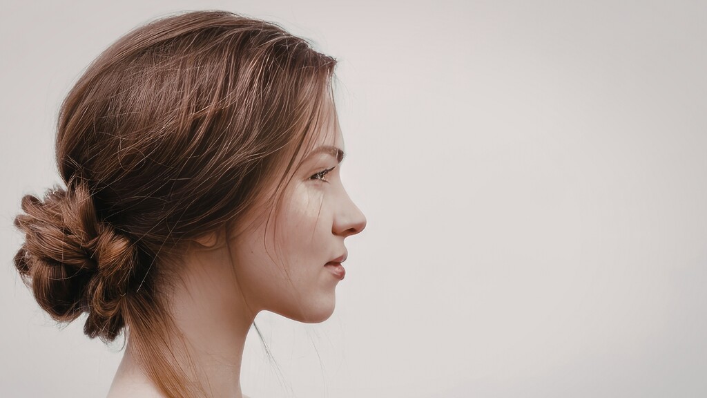 Woman with brown hair styled in a soft low bun, shown in side profile against a neutral background.
