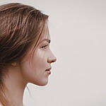 Woman with brown hair styled in a soft low bun, shown in side profile against a neutral background.