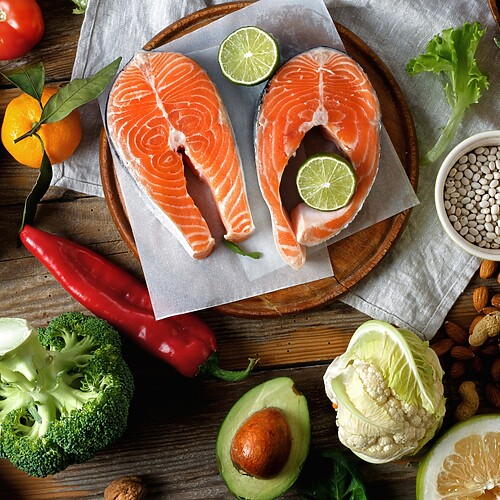 Fresh hormone balancing foods including salmon, avocado, broccoli, beans, lentils, nuts, and leafy greens on a wooden table.